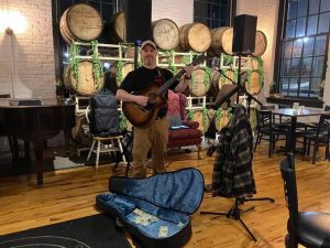 Jeremiah Williams performing acoustic guitar in front of wooden barrels
