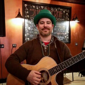 Jeremiah Williams wearing a green hat and holding an acoustic guitar