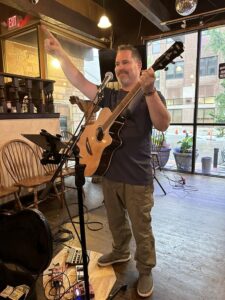 Jeremiah Williams singing and playing acoustic guitar with one arm raised